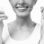 Portrait of a beautiful woman with braces on teeth cleaning teeth using dental floss isolated on a white background